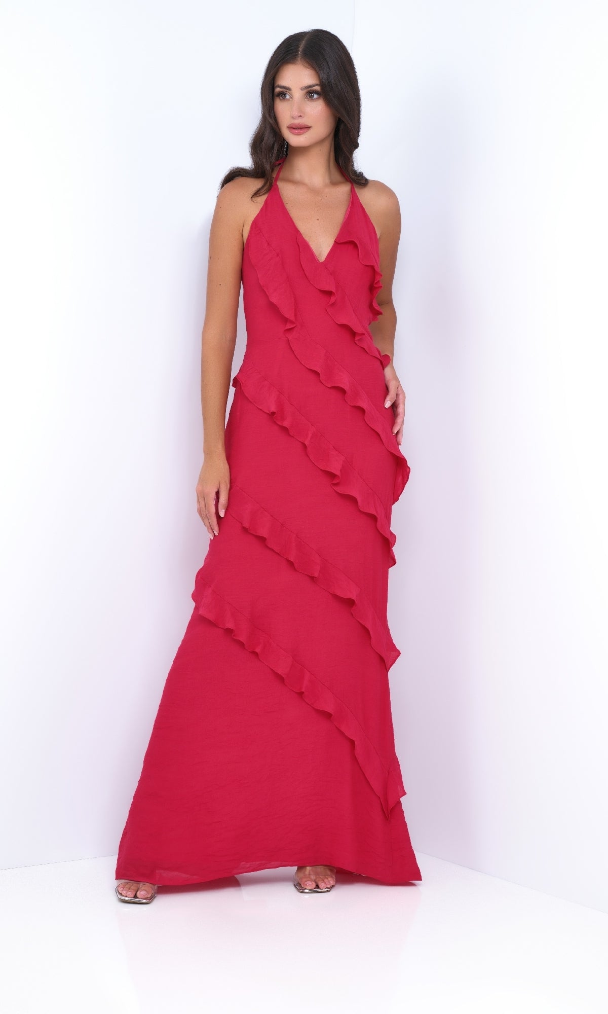 A woman models the Remi by Velvi V-Neck Halter Ruffled Long Prom Dress in red, featuring diagonal ruffle details, set against a plain white background.